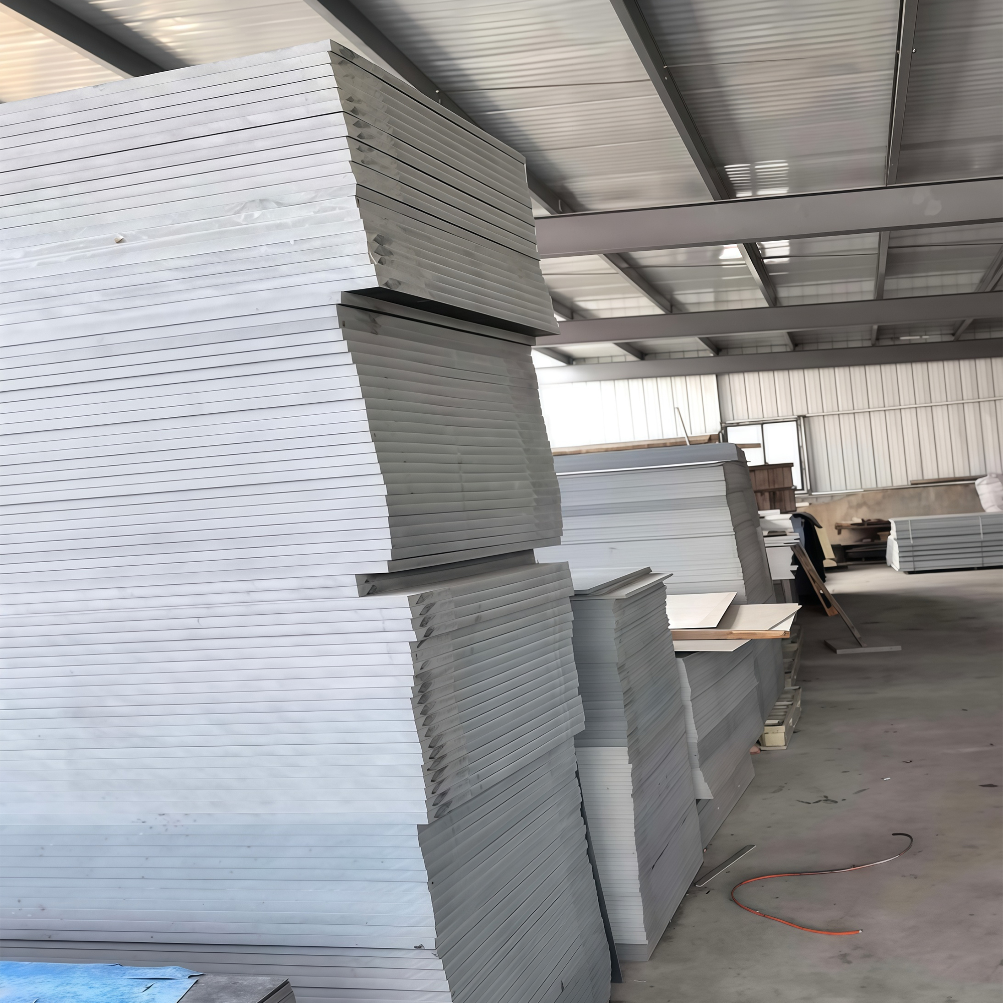 Tall stacks of grey rigid sheet stored inside a steel-framed hall